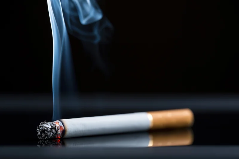 Lit cigarette with rising smoke resting on a reflective black surface