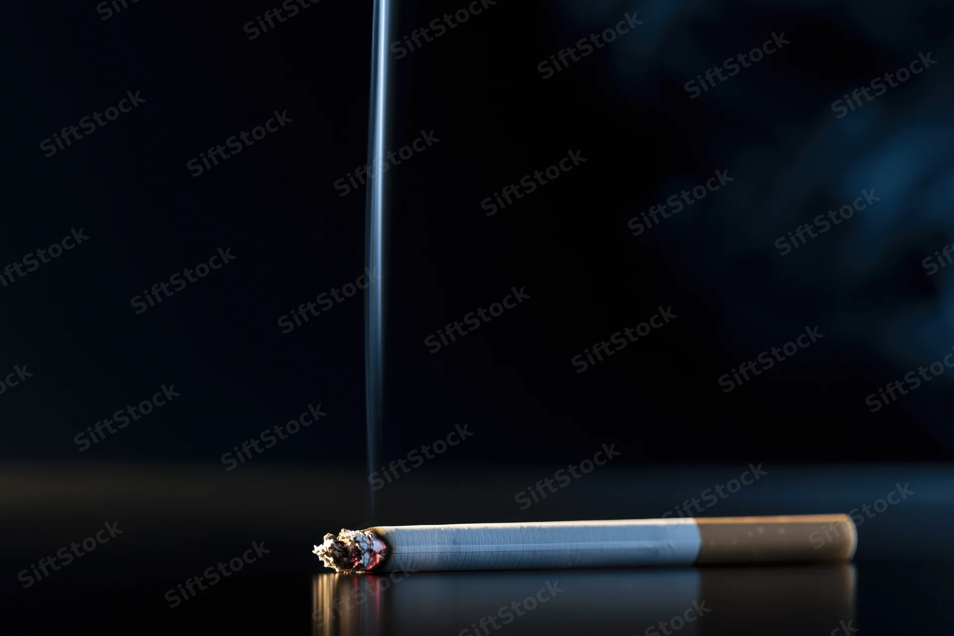 Lit cigarette with smoke rising, resting on reflective dark surface