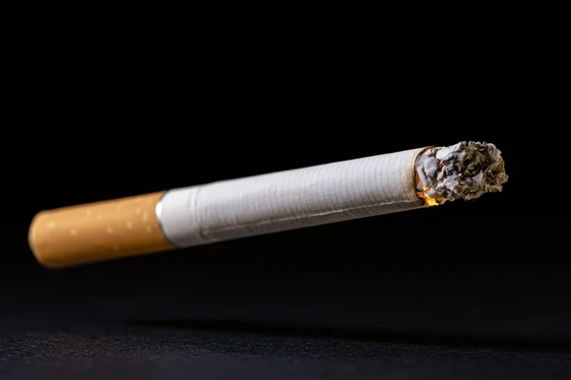 Lit cigarette burning with ash and flame suspended against black background