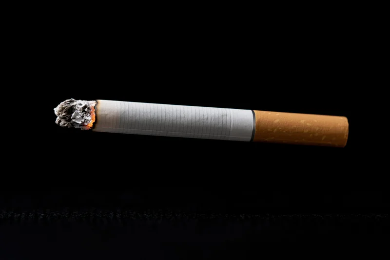Lit cigarette burning horizontally against black background
