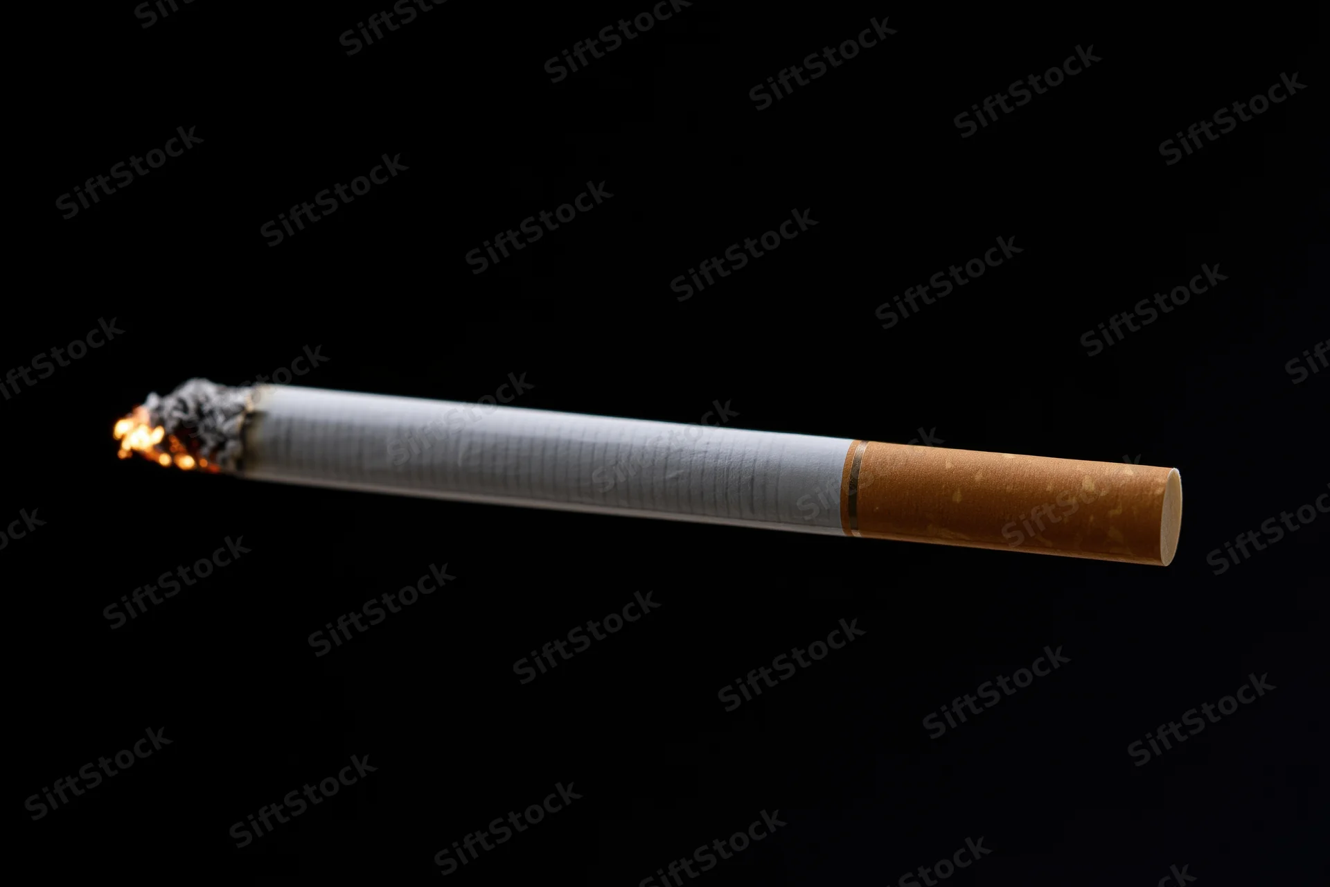 Lit cigarette burning horizontally against black background