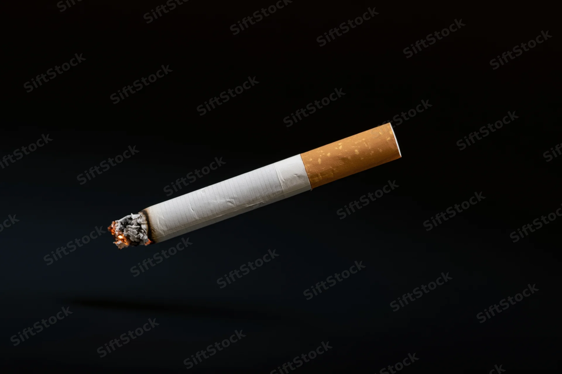 Lit cigarette suspended horizontally against black background