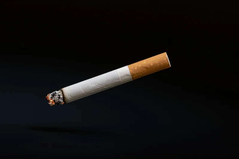 Lit cigarette suspended horizontally against black background