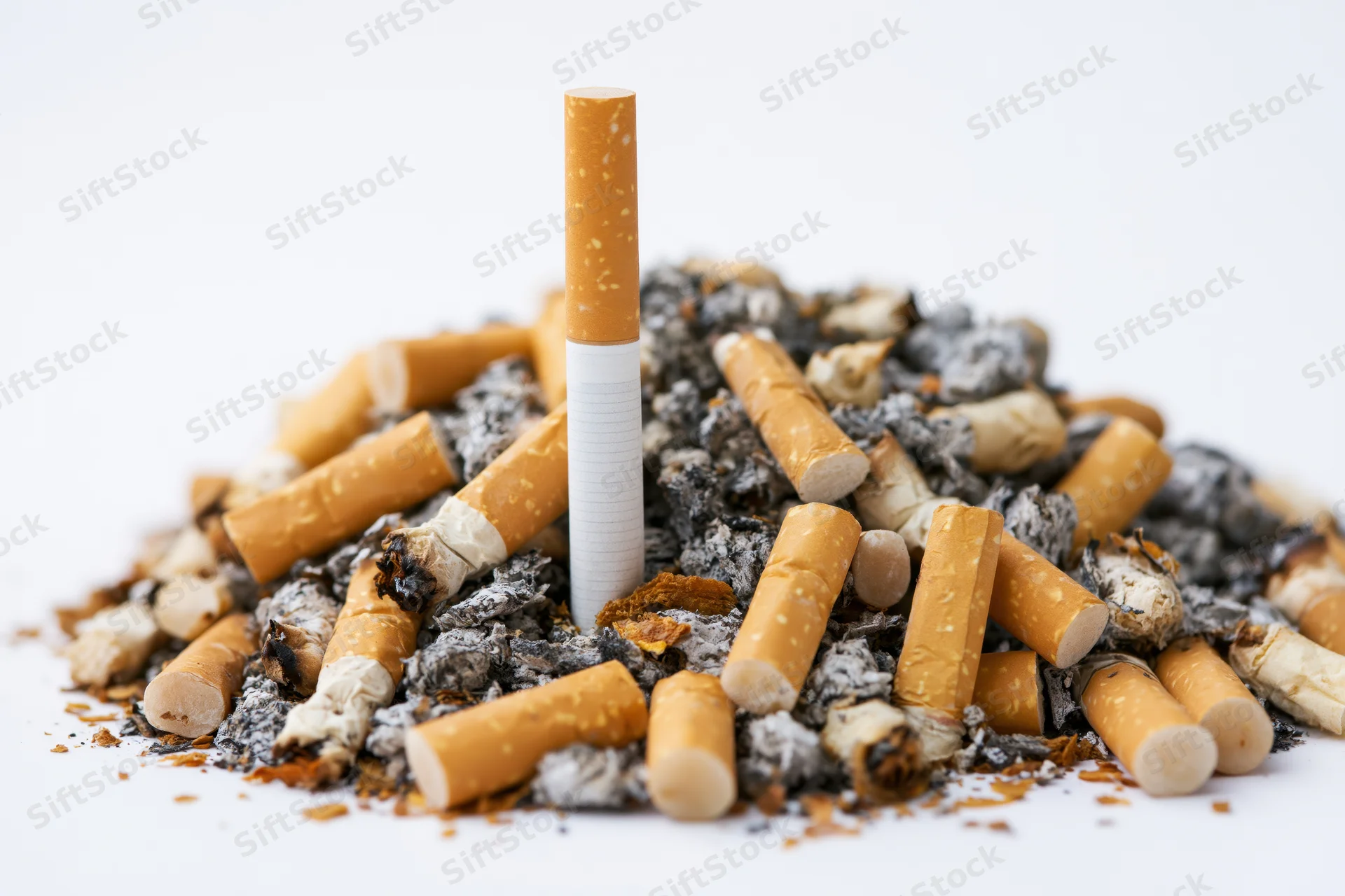 Unlit cigarette standing upright in a pile of cigarette butts and ash on white background
