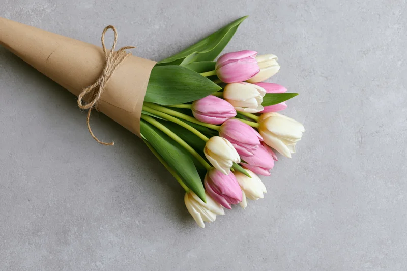 Small bouquet of pink and white tulips wrapped in kraft paper with twine on gray surface