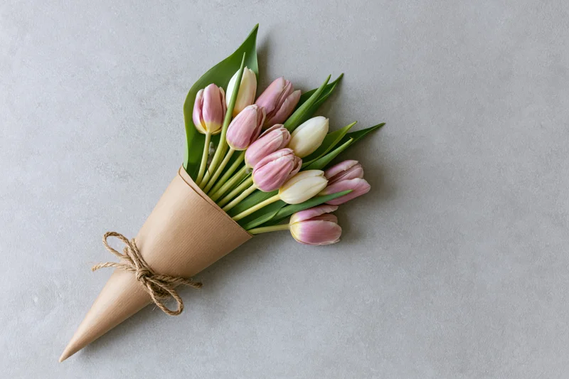 Small bouquet of pink and white tulips wrapped in kraft paper with twine bow on gray surface