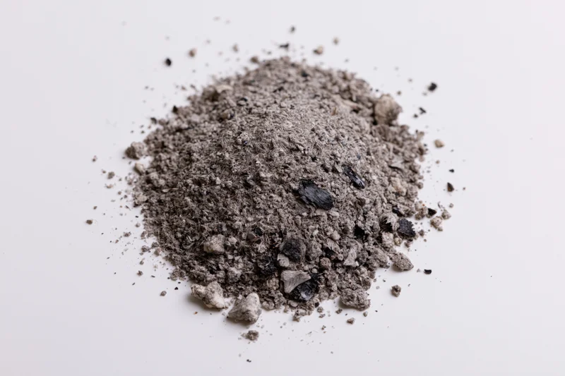 A small pile of grey and black ash debris scattered on a white surface