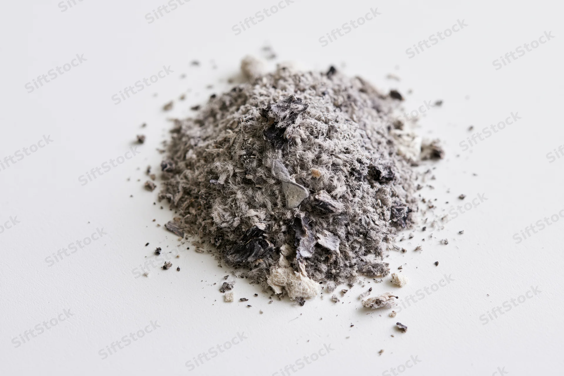 A small pile of grey and black ash debris scattered on a white surface