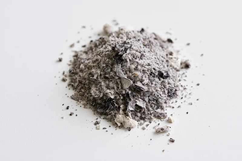 A small pile of grey and black ash debris scattered on a white surface
