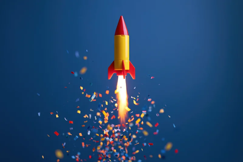 Toy rocket launching upward with bright flame and colorful confetti against blue background