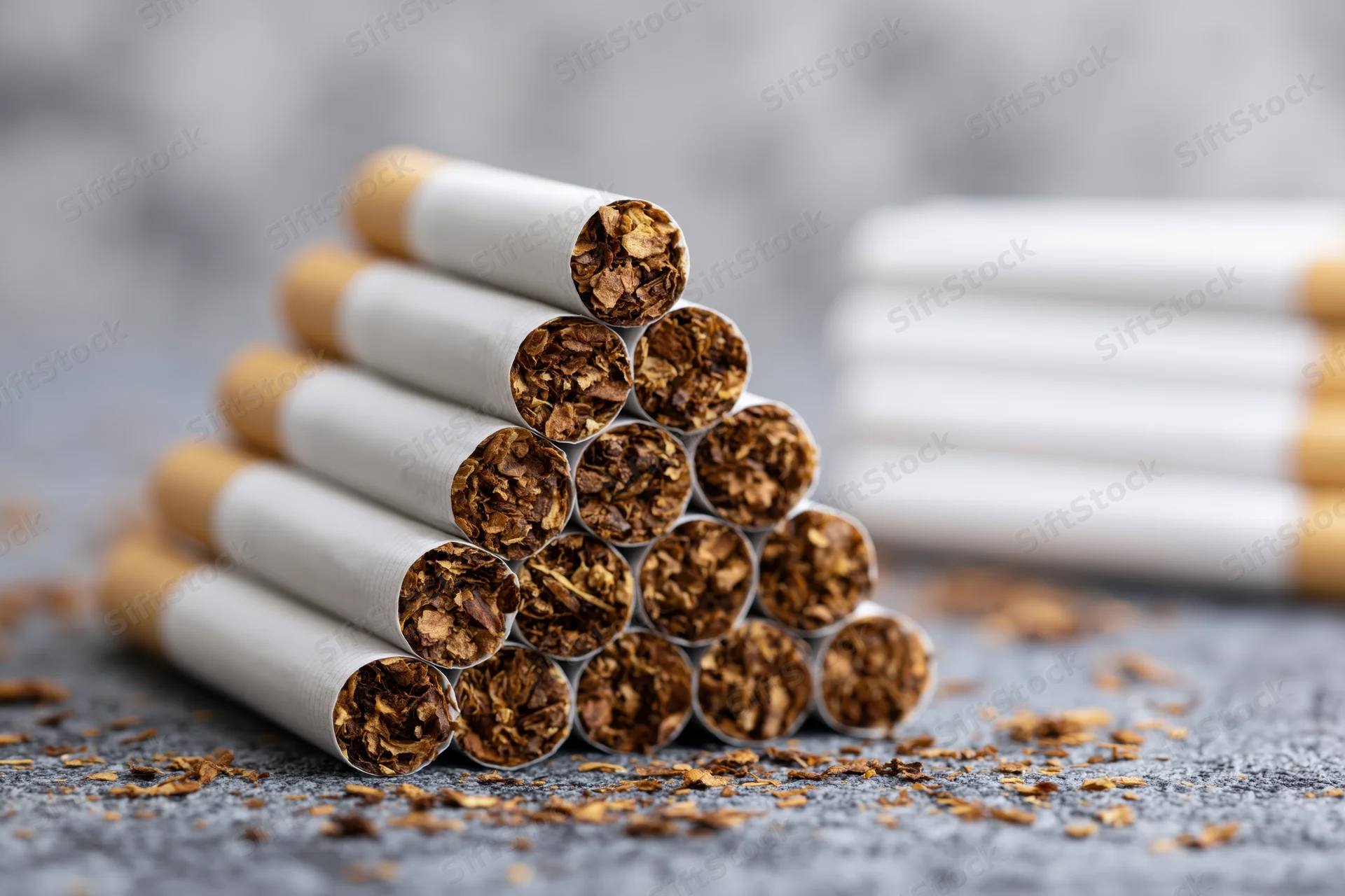 Cigarettes stacked in pyramid formation on textured surface with tobacco debris scattered around