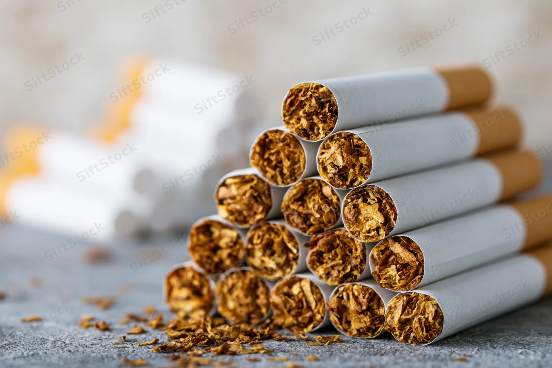 Stack of unlit cigarettes arranged in pyramid formation on textured surface