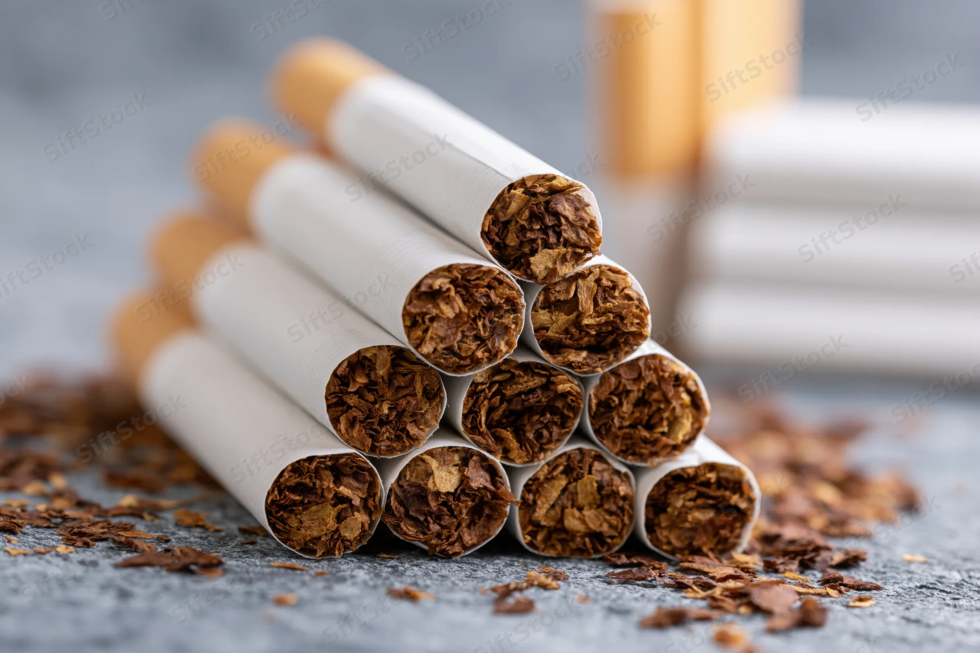 Unlit cigarettes arranged in a pyramid on a gray textured surface with scattered tobacco debris