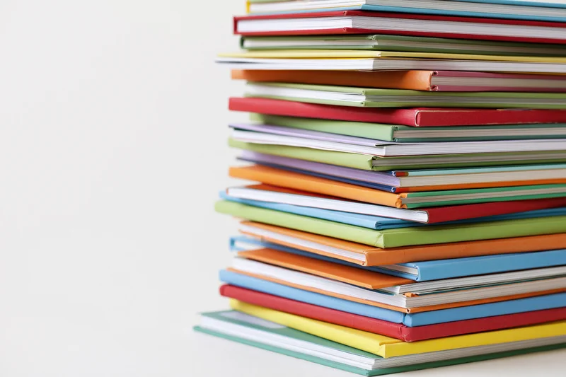 Tall stack of colorful childrens books arranged vertically on white surface