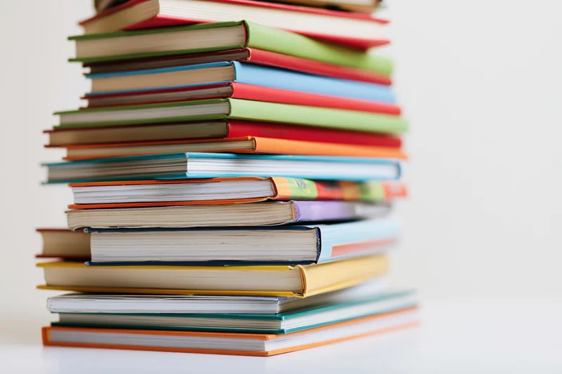 Tall messy stack of colorful childrens hardcover and paperback books on white surface