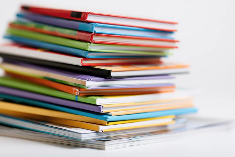 Tall messy stack of colorful childrens hardcover and paperback books on white surface