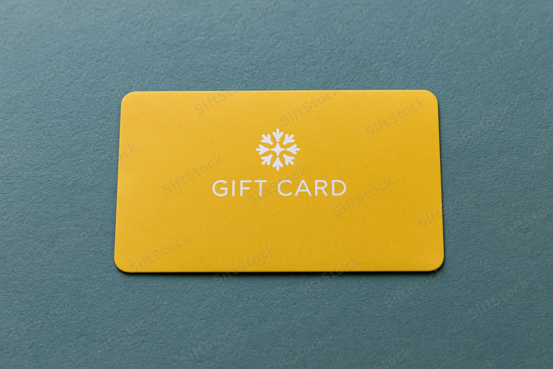 Yellow gift card with snowflake logo lying flat on textured teal surface