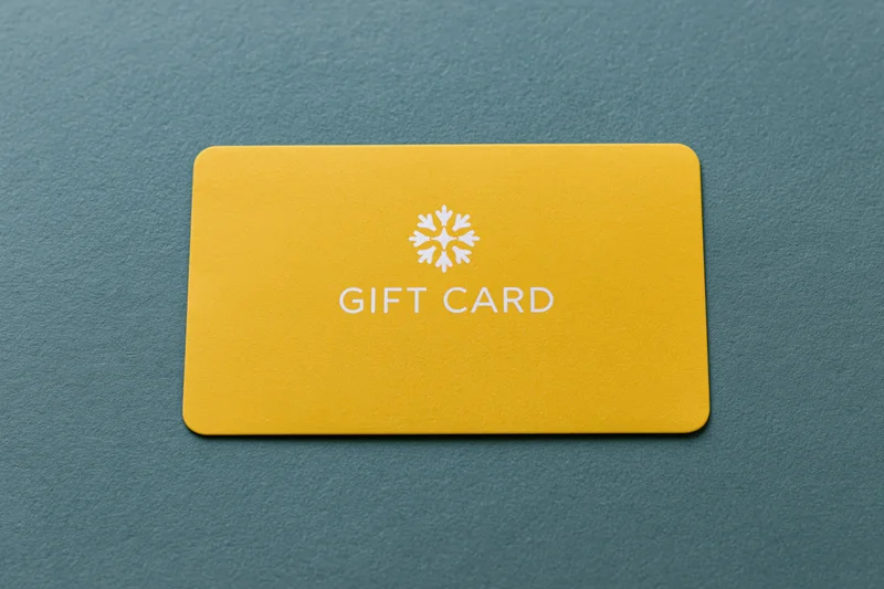 Yellow gift card with snowflake logo lying flat on textured teal surface