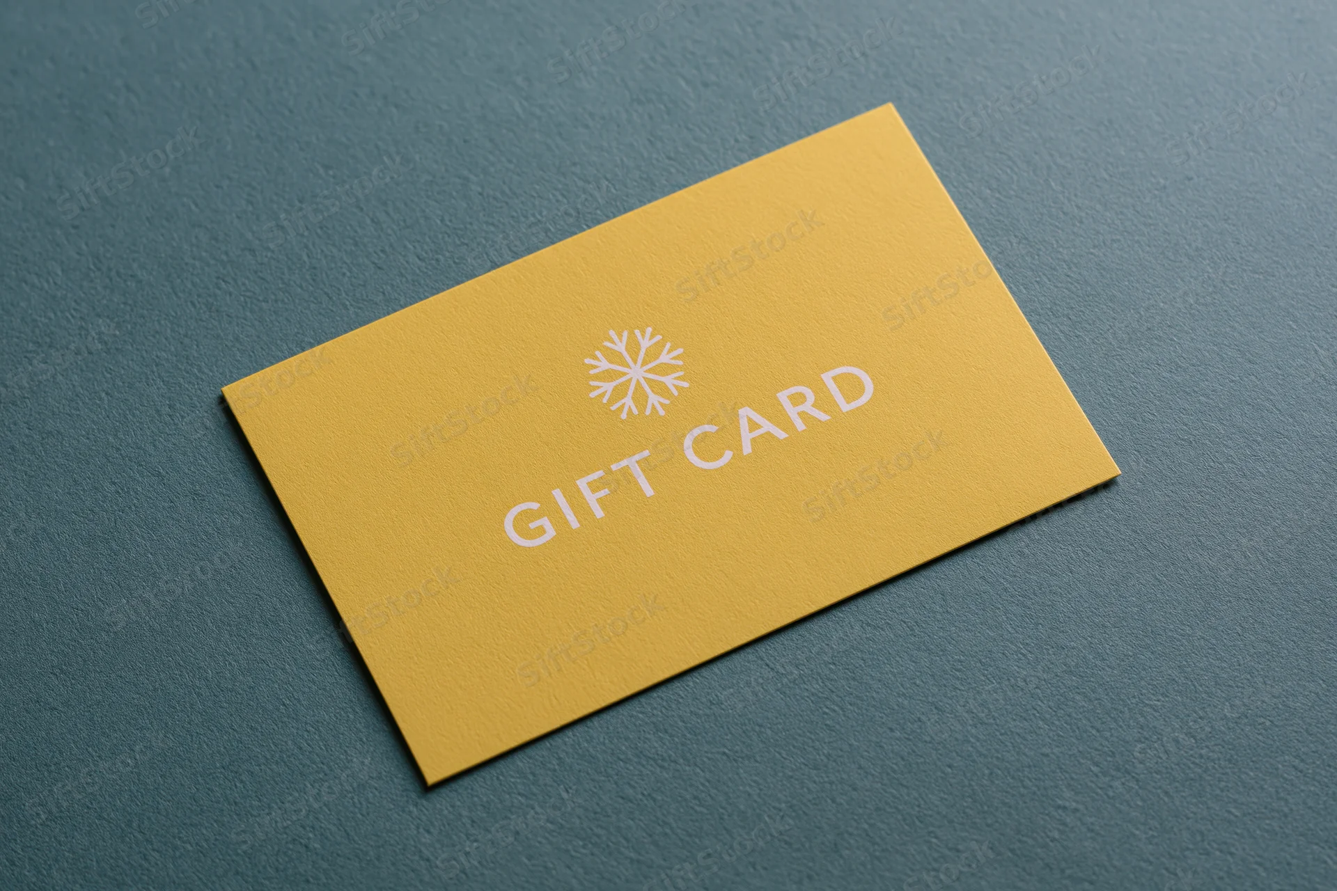Yellow gift card with snowflake design lying flat on textured teal surface