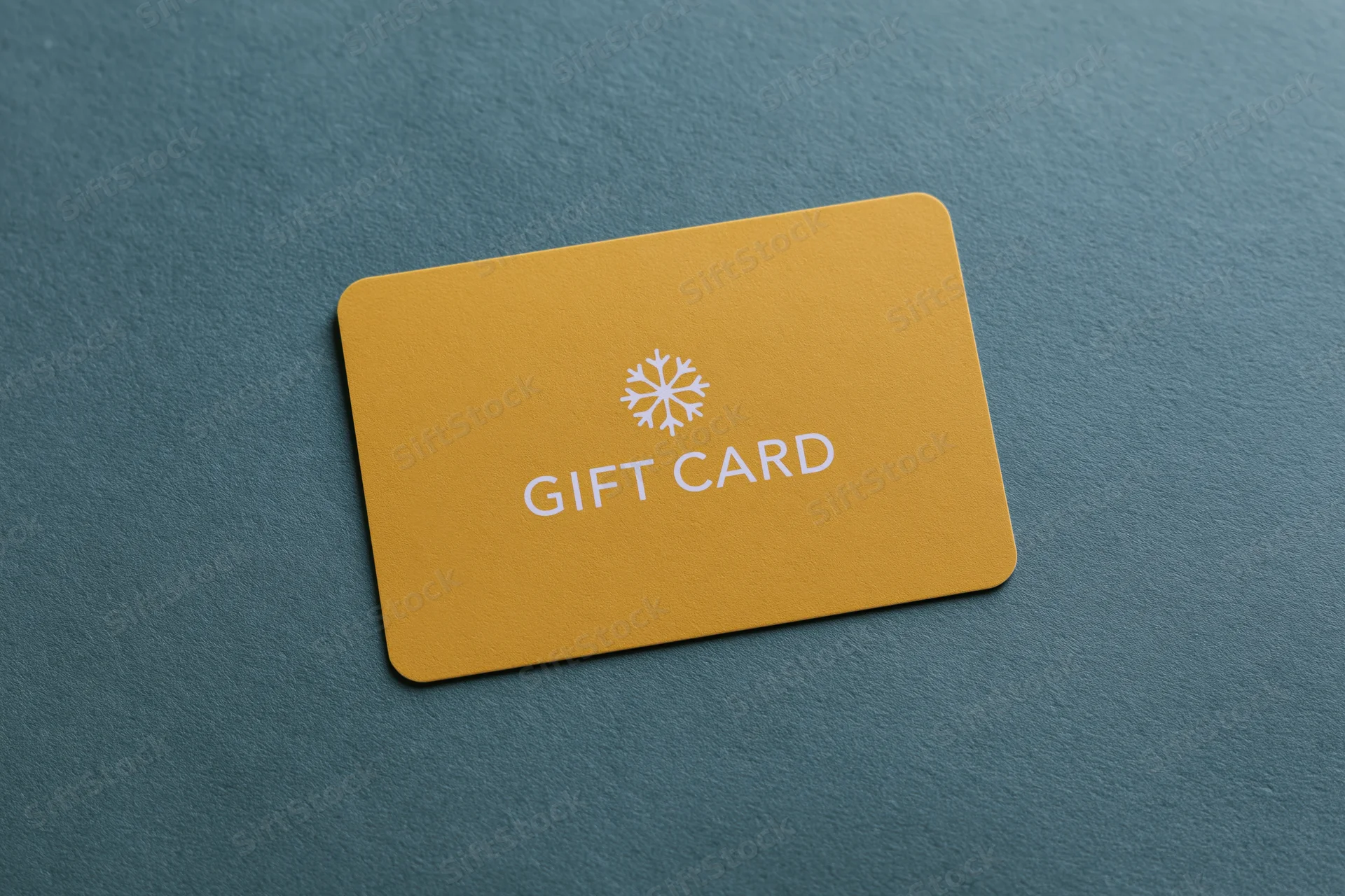 Yellow gift card with snowflake logo lying flat on textured teal surface