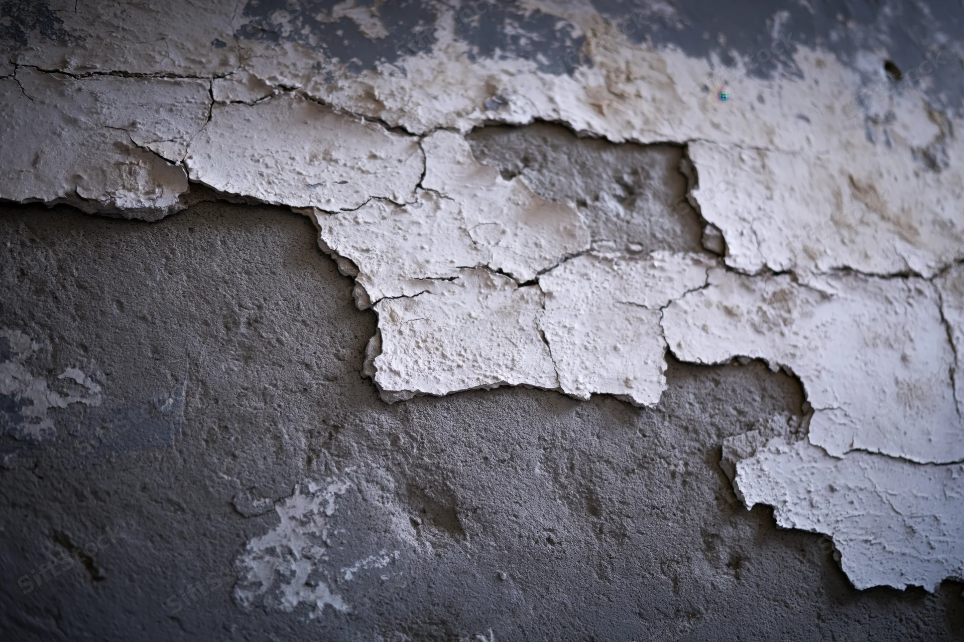 Peeling white plaster on a cracked concrete wall in an abandoned interior