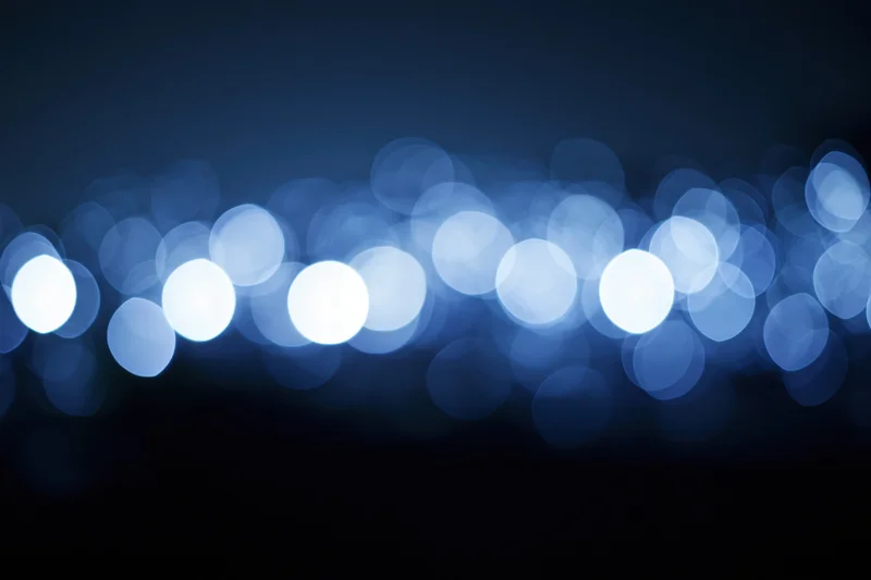 Abstract bokeh background with out-of-focus blue light circles against dark gradient