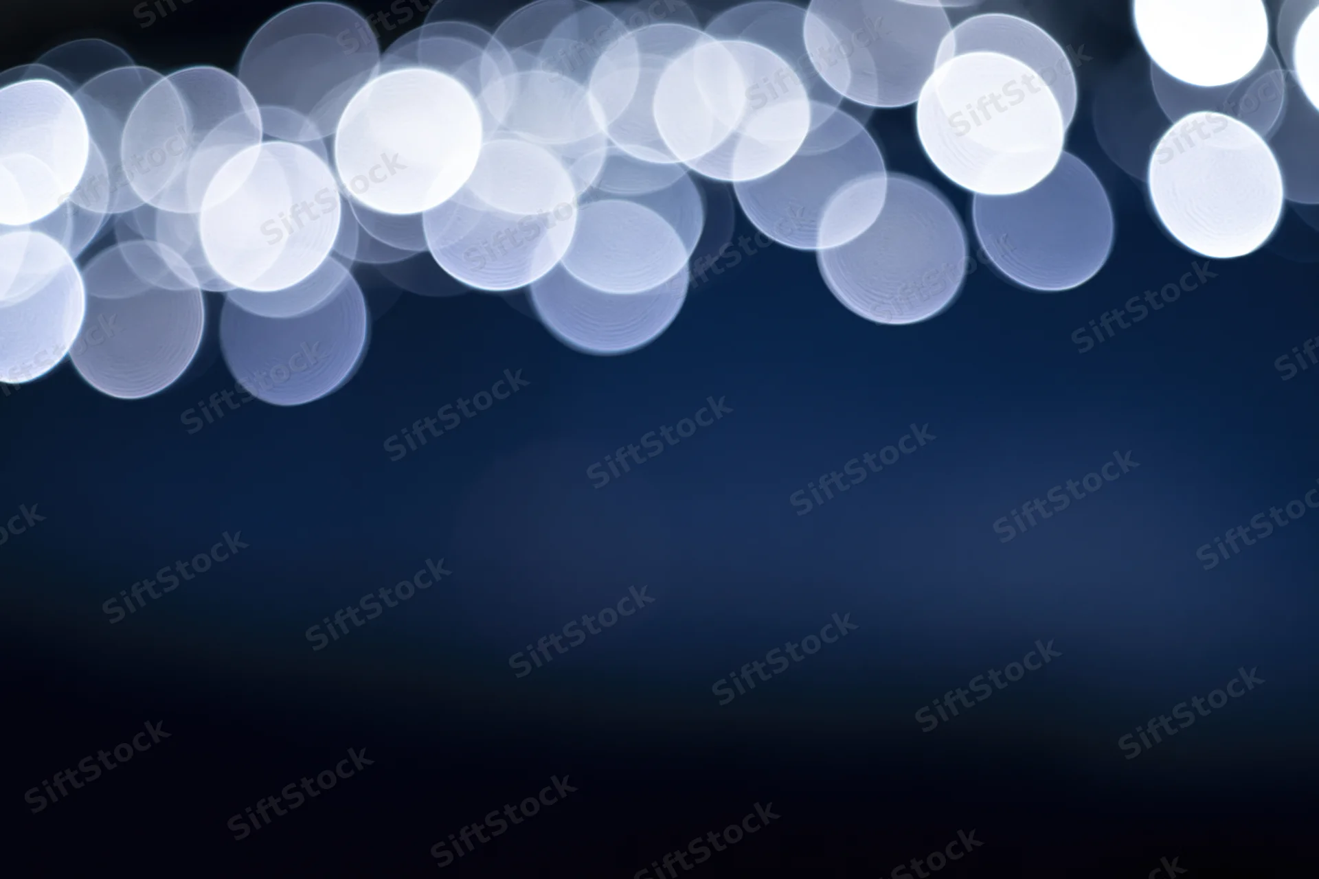 Abstract bokeh lights in soft white circles against a dark blue gradient background with copyspace below