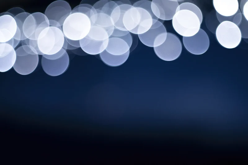 Abstract bokeh lights in soft white circles against a dark blue gradient background with copyspace below