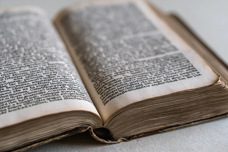 Open aged book with dense text pages lying flat on a light surface