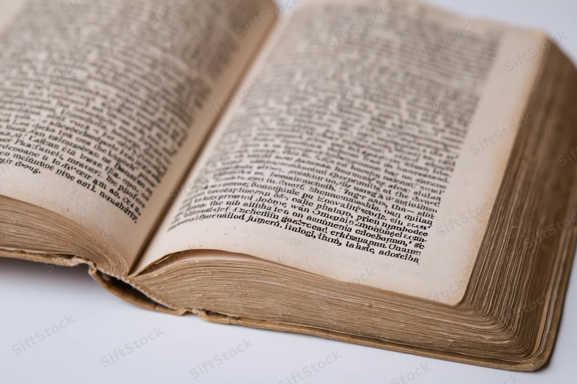 Open aged book with dense printed text on yellowed pages against white background