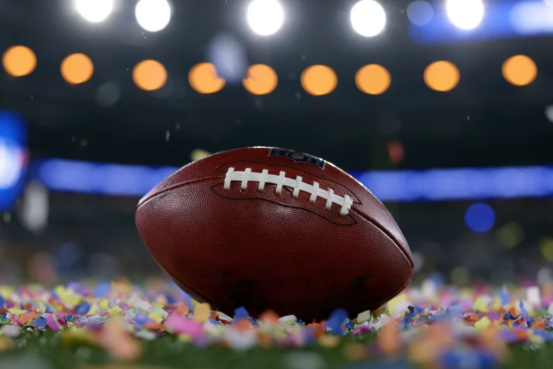 Nfl football resting on turf covered in confetti under stadium lights at night