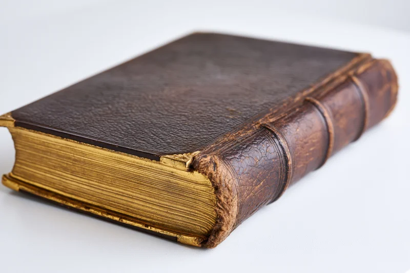 Antique leather-bound book resting at an angle on a white surface