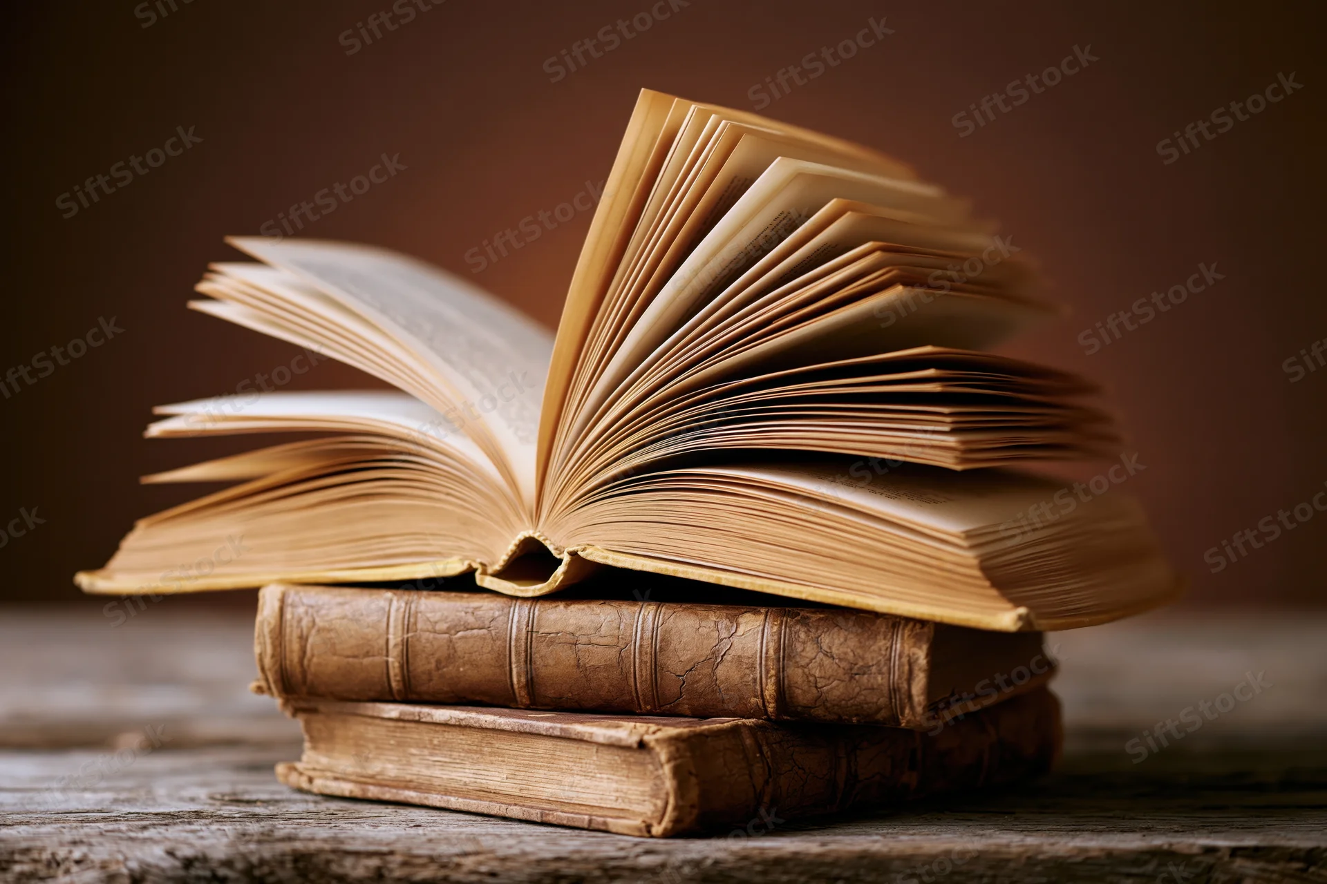 Open vintage book resting on a stack of old leather-bound books on a wooden surface