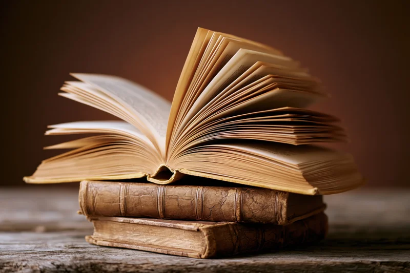 Open vintage book resting on a stack of old leather-bound books on a wooden surface