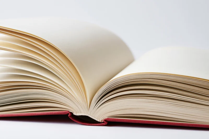 Open hardcover book with fanned pages and red binding on white background