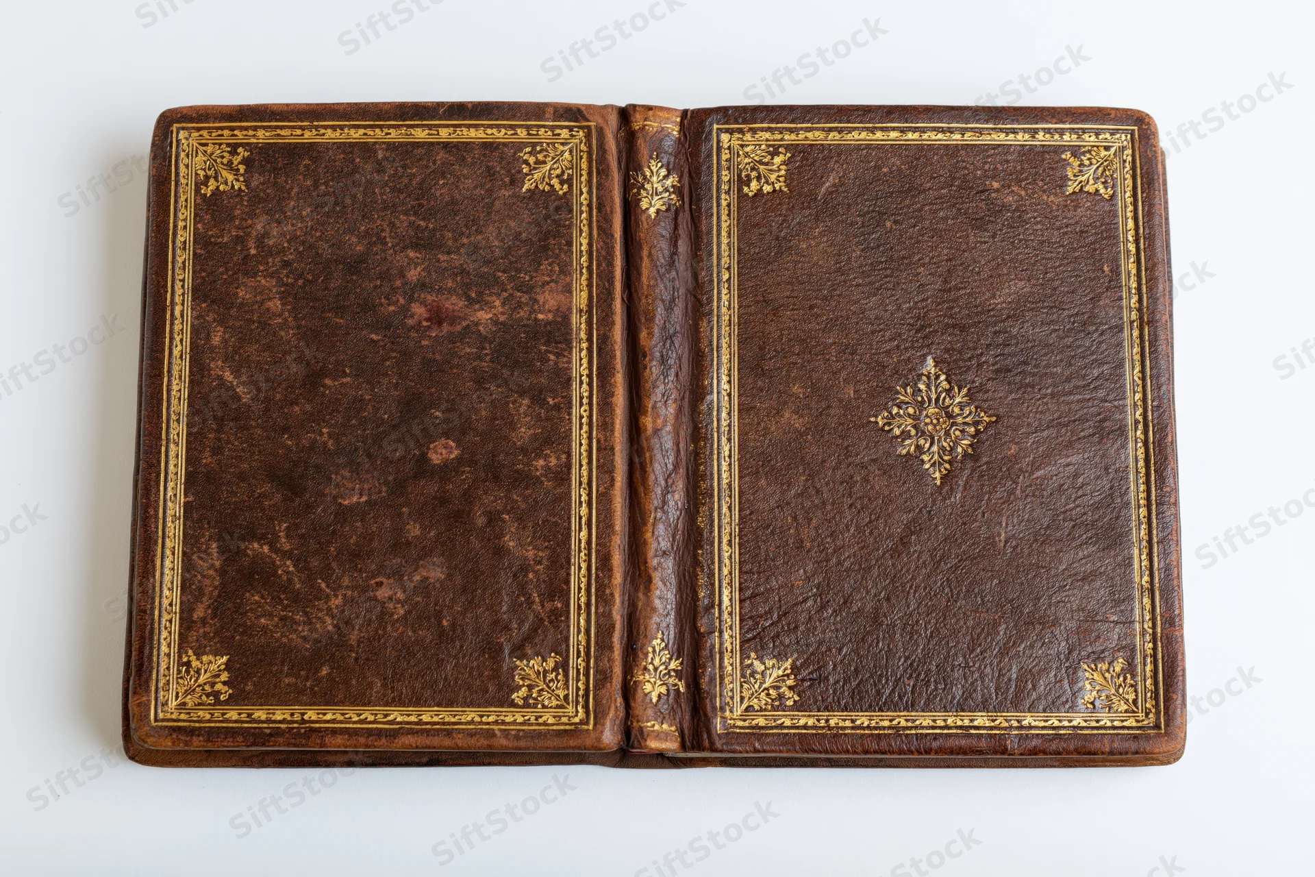 Open antique leather book with gold embossed decoration on white background