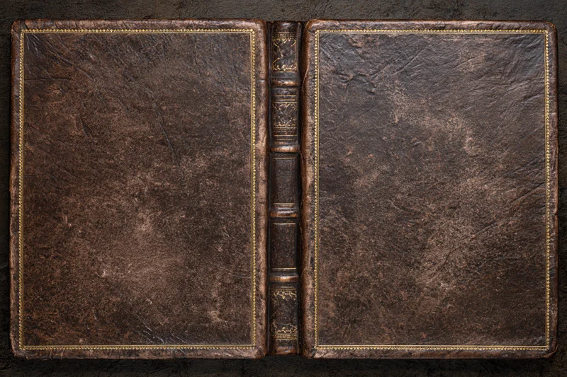 Open antique leather-bound book laid flat showing both covers on dark surface