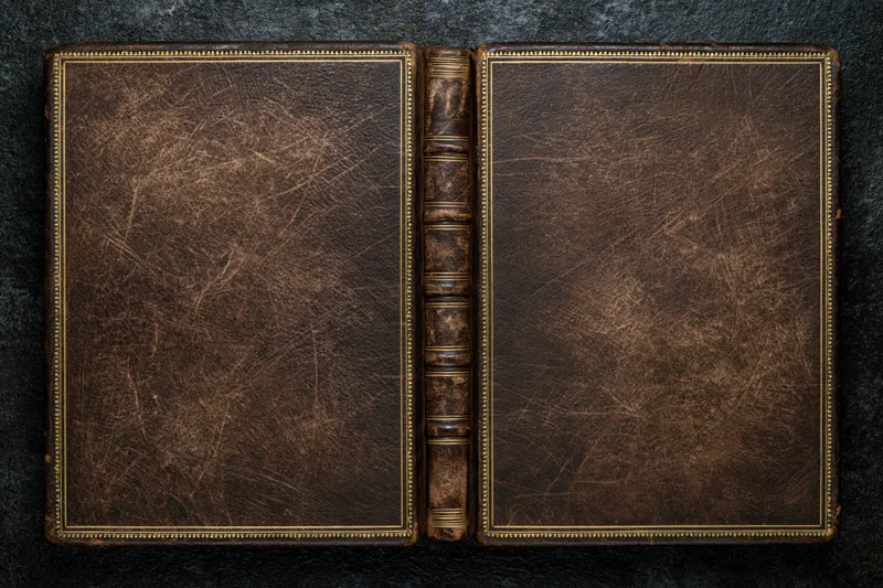Open antique leather-bound book laid flat showing both covers on dark surface