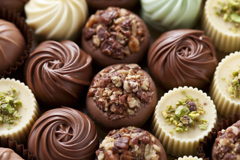 Assorted luxury chocolate pralines and truffles arranged tightly in paper liners with nuts and swirls