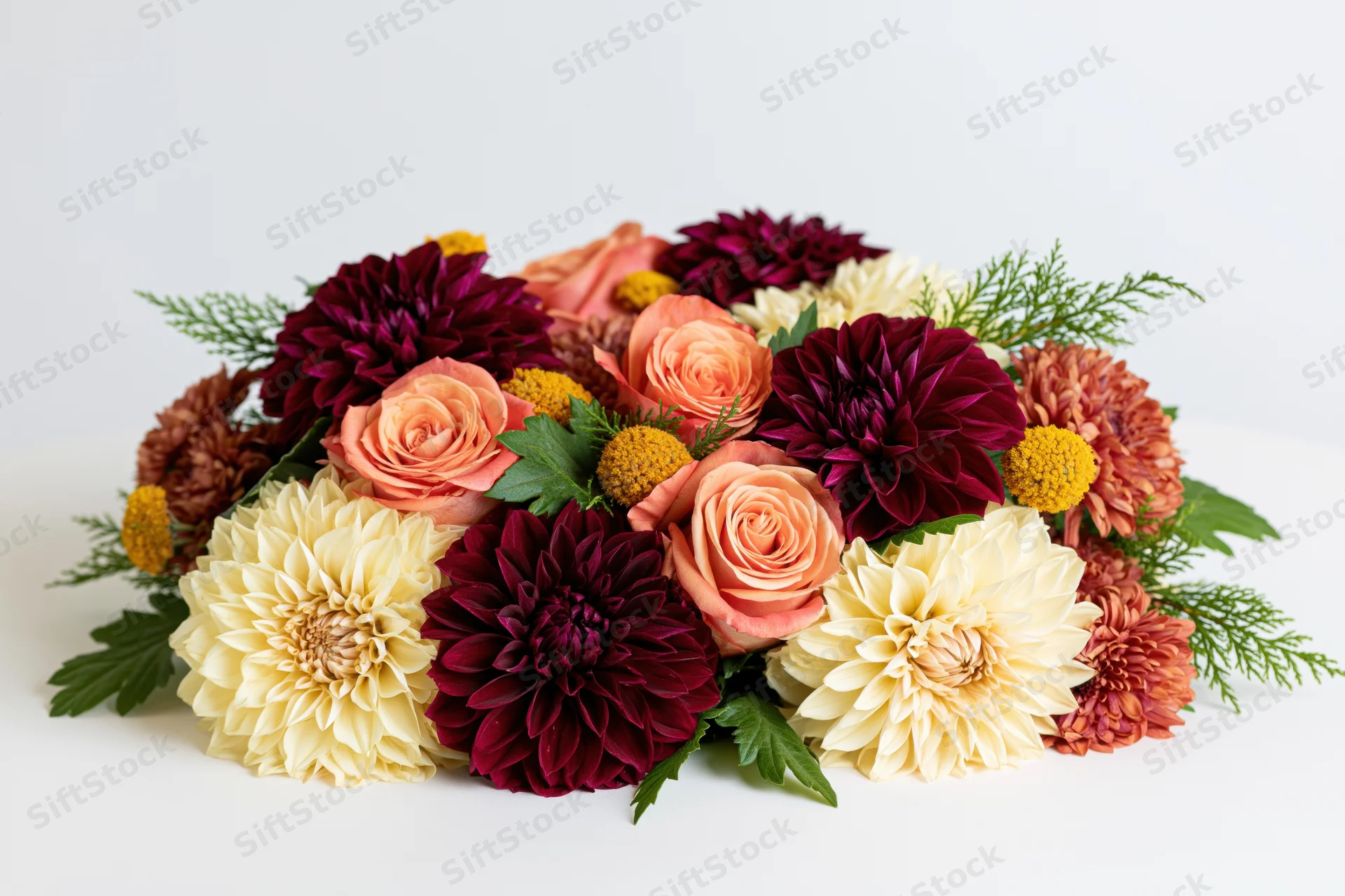 Autumn floral arrangement with dahlias, roses, and greenery on white surface
