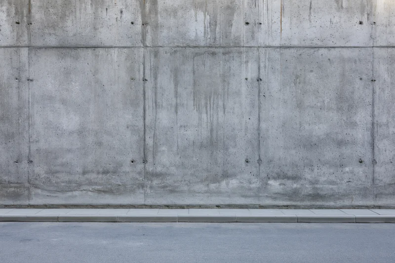 Wide view of a bare concrete wall with visible seams and stains along a sidewalk