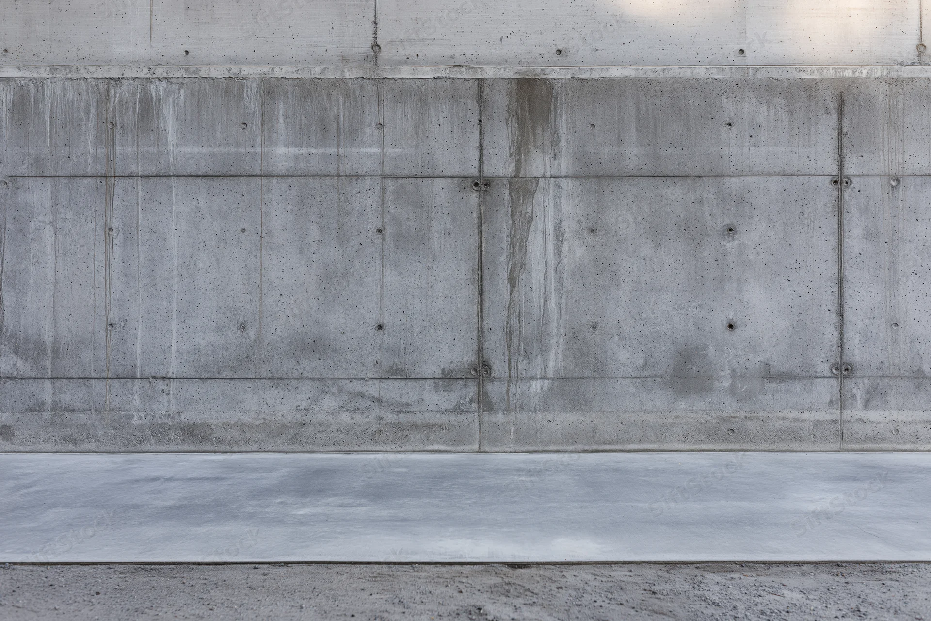 Wide flat view of a bare concrete wall with horizontal seams and embedded bolts, exterior building surface
