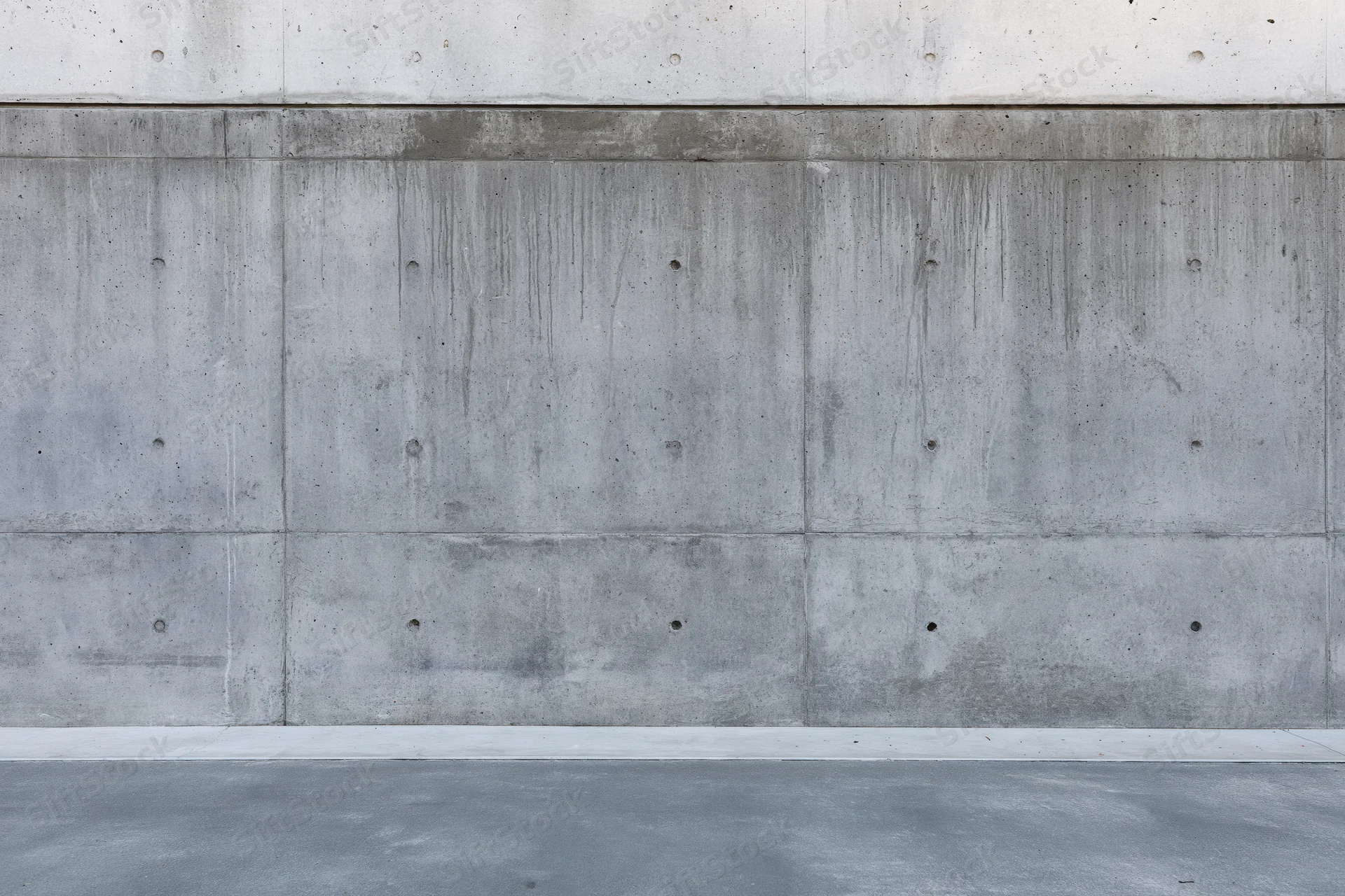 Wide flat view of a bare concrete wall with visible seams and formwork holes, exterior building surface