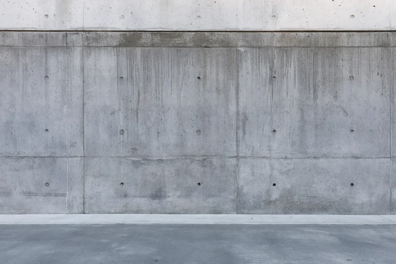 Wide flat view of a bare concrete wall with visible seams and formwork holes, exterior building surface