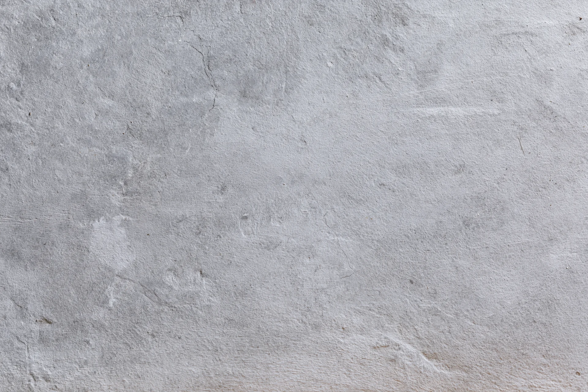 Close-up of a rough gray concrete wall surface with cracks and texture filling the frame