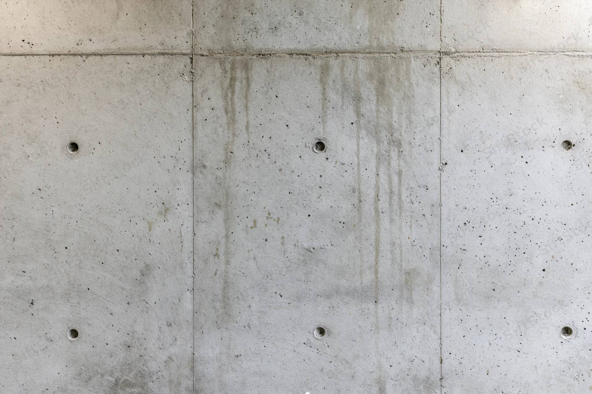Bare poured concrete wall with visible seams and circular holes, flat-on view