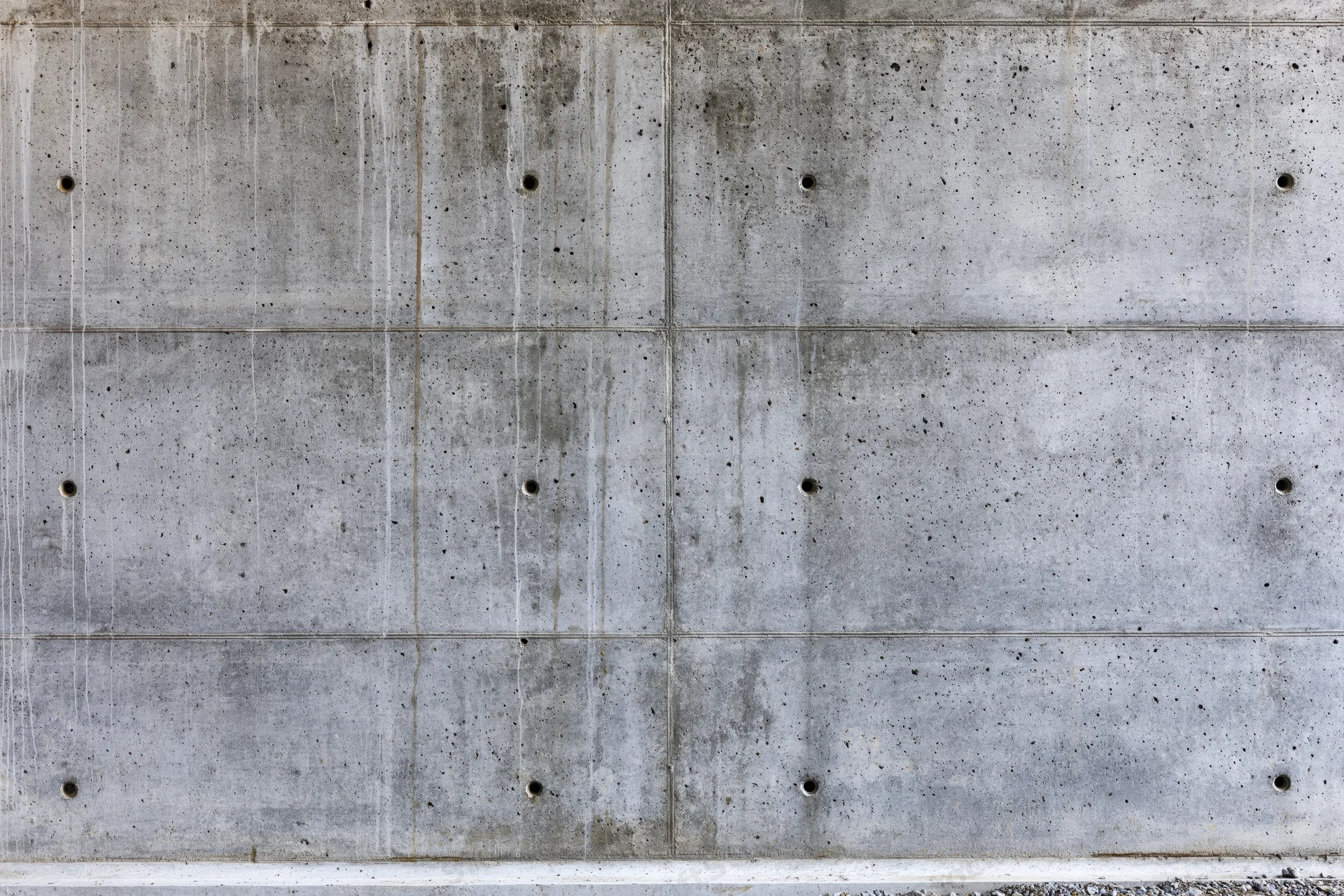 Bare poured concrete wall with grid pattern and circular holes filling the frame