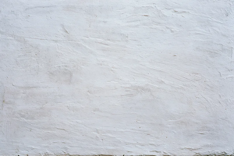 White plastered concrete wall with uneven texture and visible surface imperfections