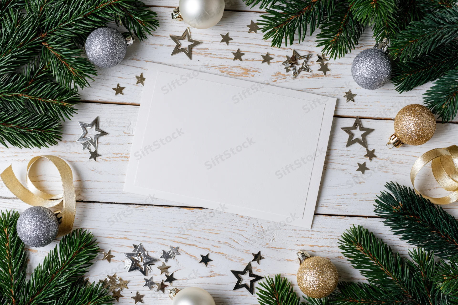 Blank white greeting card on a white wooden surface surrounded by pine branches, ornaments, and stars