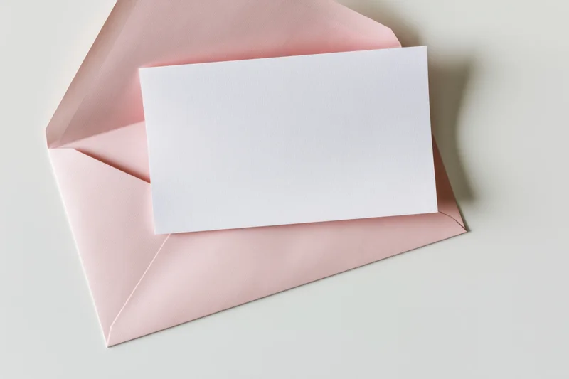 Blank white card resting on open blush pink envelope on white surface